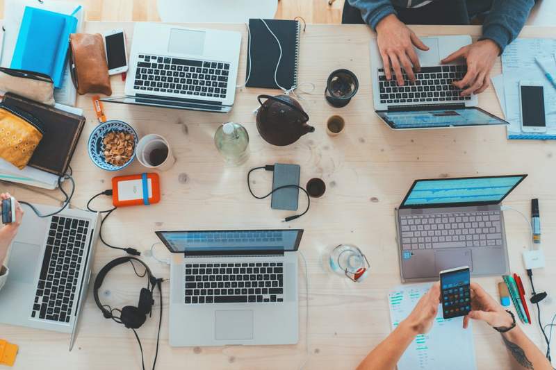 Mesa vista de cima com vários laptops e anotações